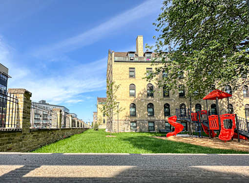 A playground with a red slide is in front of a large building.