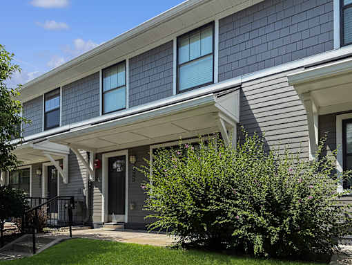 A house with a grey facade and a green bush in front.