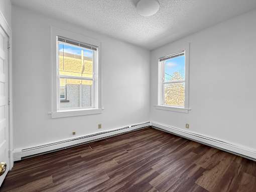 A room with white walls and wood flooring with two windows.