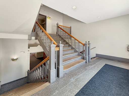 A staircase with a wooden handrail and a metal balustrade leads up to a landing with a door.