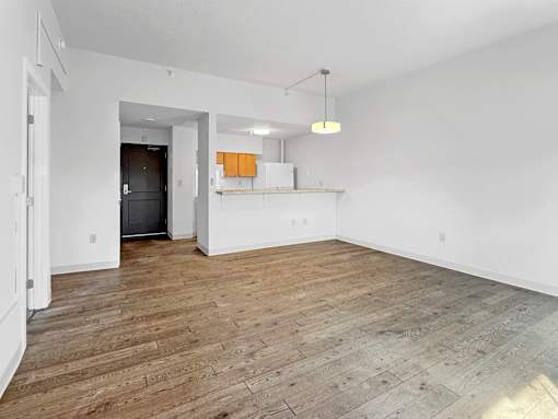 A room with wooden flooring and a kitchenette in the background.
