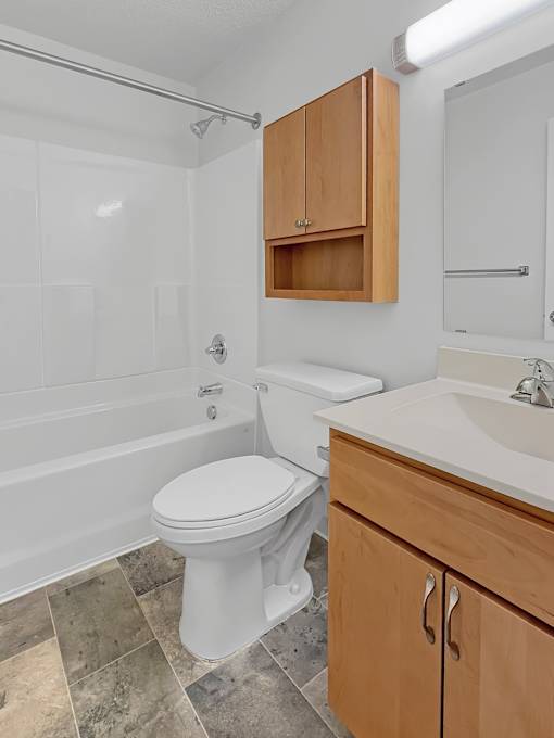 A white toilet in a bathroom with a wooden cabinet above it.
