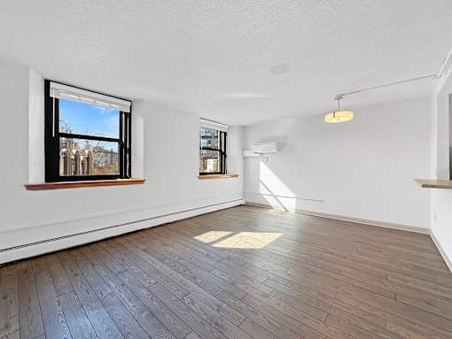 A room with wooden flooring and two windows.