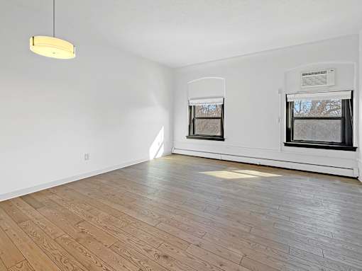 A room with wooden flooring and two windows.