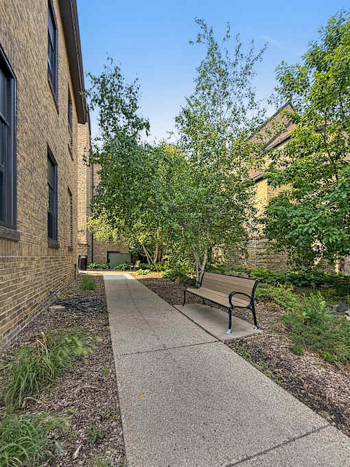 A bench sits on a sidewalk next to a brick building.