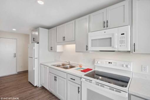 A white kitchen with a refrigerator, microwave, oven, and sink.