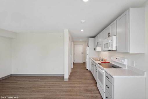 A kitchen with white cabinets and a wooden floor.