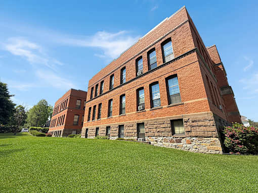 A red brick building with a stone foundation and a green lawn in front.