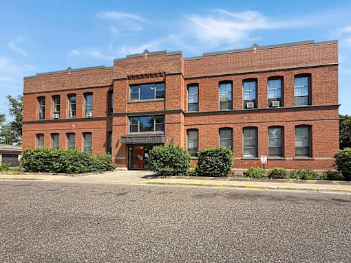 A red brick building with a black awning and a parking lot in front.