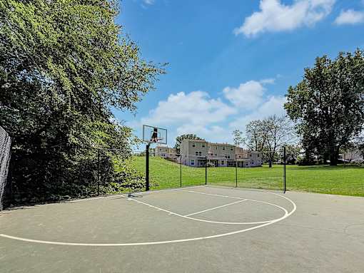 A basketball court surrounded by trees and a building in the background.