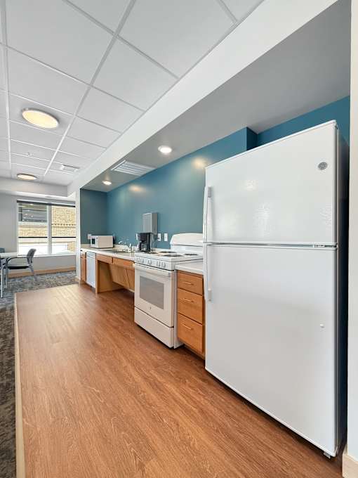 A white refrigerator stands in a kitchen with wooden floors and white walls.