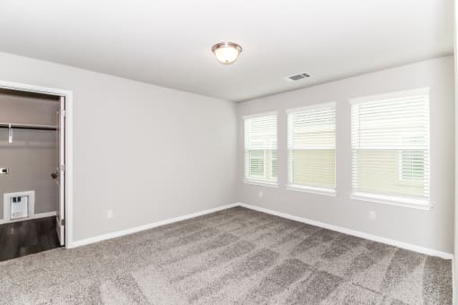 an empty bedroom with three windows and a closet