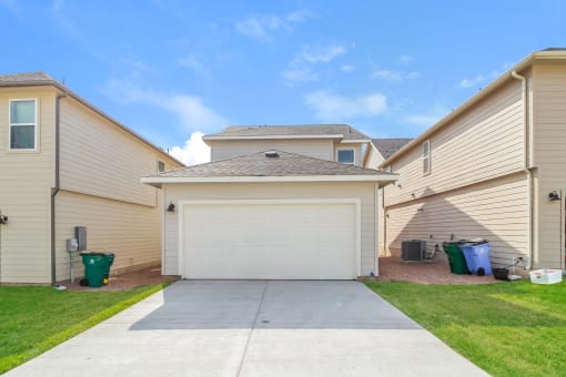 a driveway with a garage door and a house in the background
