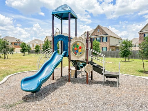 a playground with a slide and other toys in a yard with houses in the background