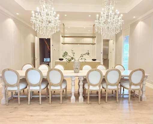 A large dining table with white chairs and a chandelier hangs in a spacious room.