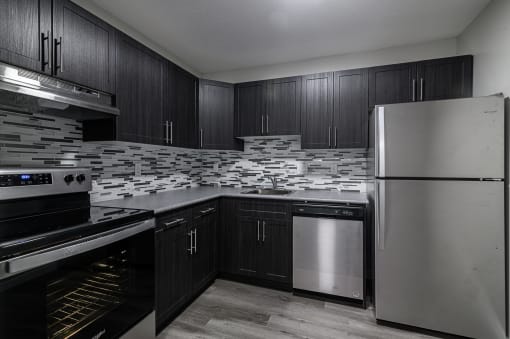 a black and white photo of a kitchen with black cabinets and stainless steel appliances