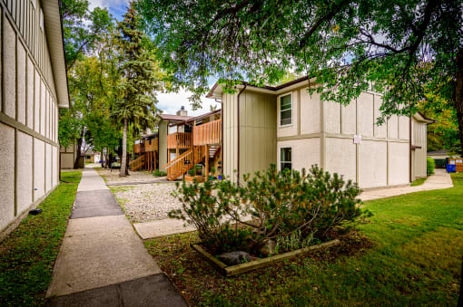 a sidewalk between two buildings with trees and grass