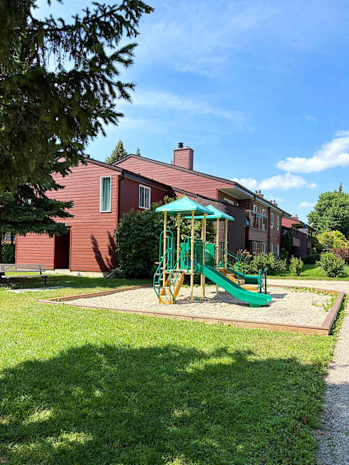 A playground with a green slide and a red building in the background.