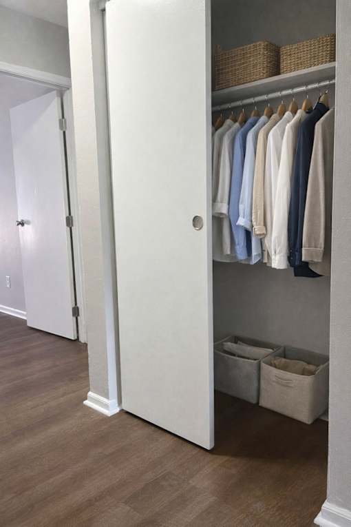 A white closet with clothes hanging and baskets on the shelf.