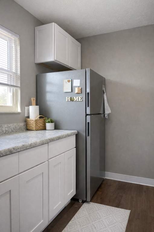 A kitchen with a grey fridge and white cabinets.