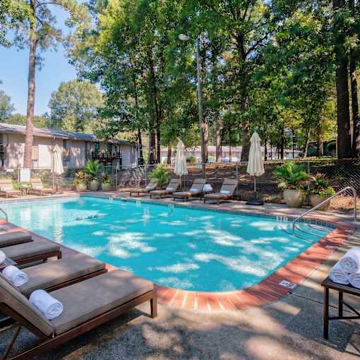 A pool surrounded by trees and lounge chairs.