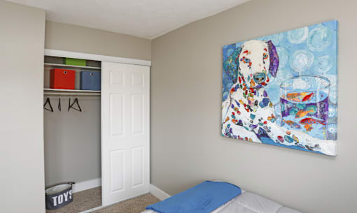 A painting of a dog with a glass of water is hanging on the wall above a bed in a room.