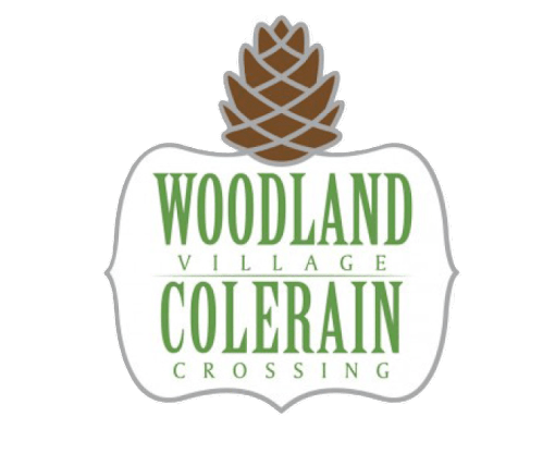 A logo with a pine cone and the words "Woodland Village Colerain Crossing".