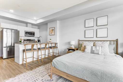 A bedroom with a bed, a kitchen area, and a dining table.