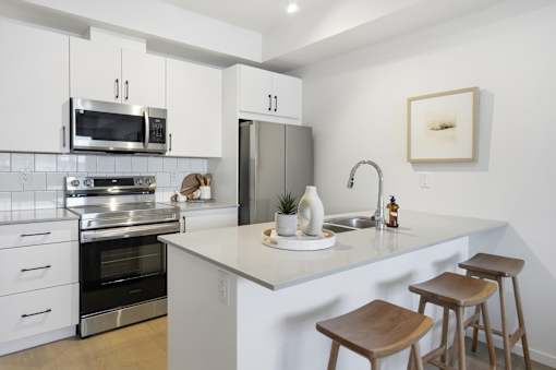 A kitchen with white cabinets and a white island with a sink and two stools.