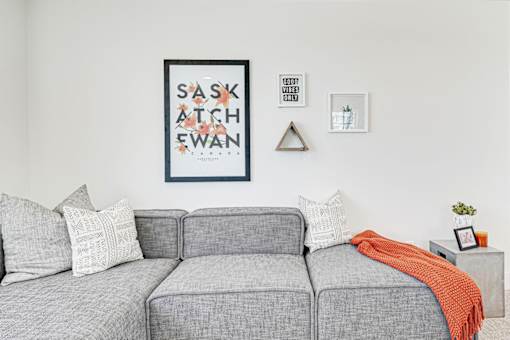 A grey couch with a red throw and a framed poster reading "Saskatchewan" on the wall behind it.