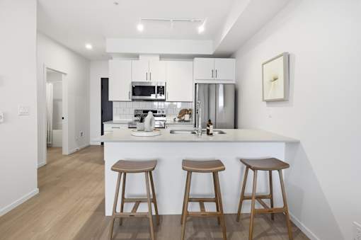 A kitchen with white cabinets and a white island with two stools.