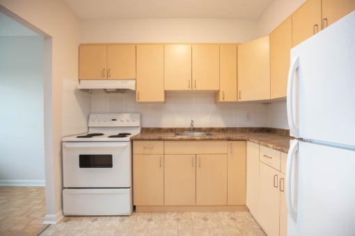 an empty kitchen with white appliances and wooden cabinets