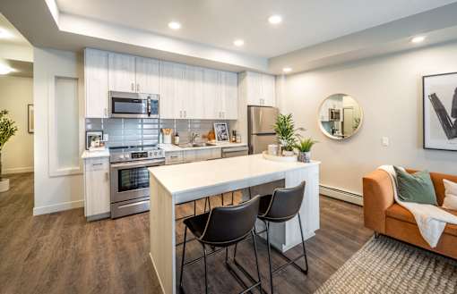 A modern kitchen with a white island and black chairs.