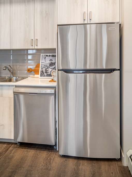 A stainless steel refrigerator stands next to a sink in a kitchen.