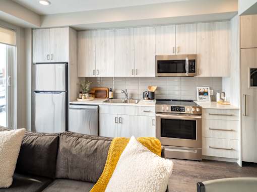 A modern kitchen with a grey couch and a yellow throw pillow.