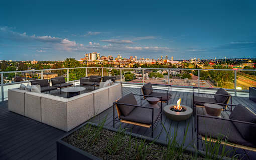 A rooftop patio with a fire pit and seating area overlooking a city skyline.
