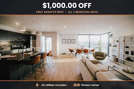 A modern living room with a kitchen area and a fitness center is advertised with a $1,000.00 off first month's rent offer for all 2 bedroom units.