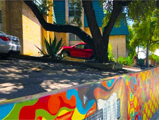 A red car is parked behind a colorful wall.