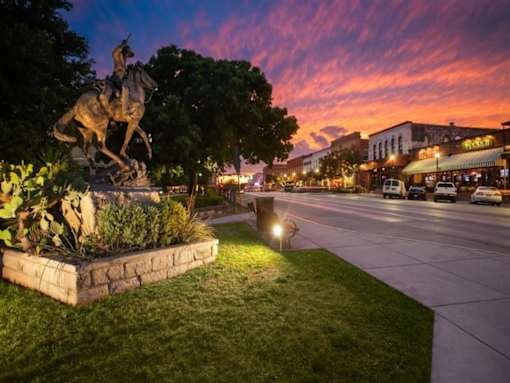 A statue of a man on a horse is illuminated by street lights at dusk.