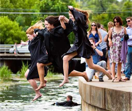 A group of people are jumping into a body of water from a dock.