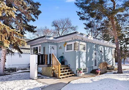 A blue house with a white door and windows is surrounded by snow.