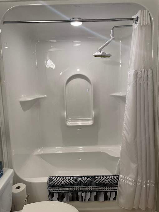A white bathroom with a toilet, a shower with a white curtain, and a black and white towel.