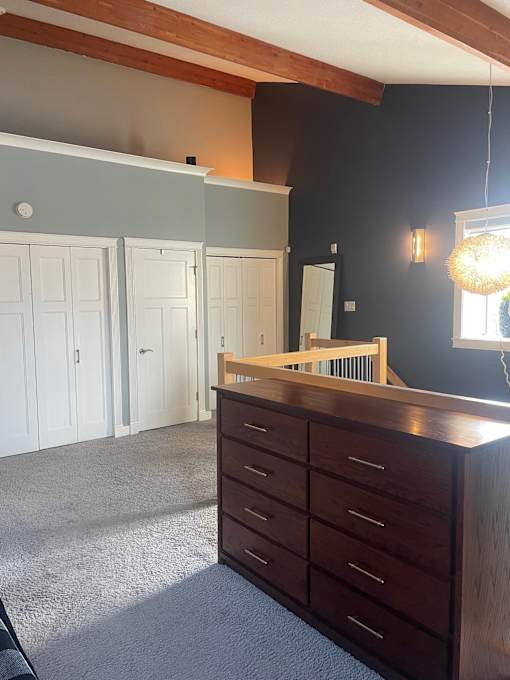 A dresser sits at the top of the stairs in a room with a grey carpet.