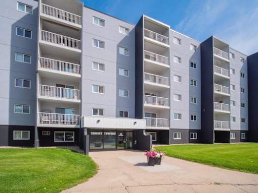 A Sunset Towers residential building with balconies and a small garden area in front.