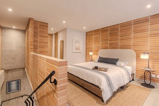 A bedroom with a bed, nightstand, and a staircase.