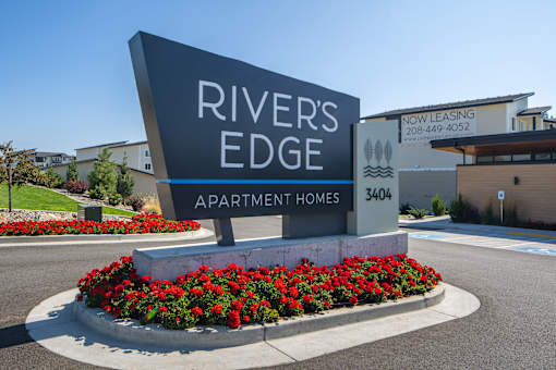 A sign for Rivers Edge Apartment Homes is surrounded by red flowers.