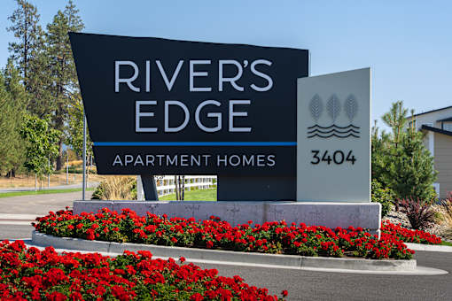 A sign for River's Edge Apartment Homes with a flower bed in front.
