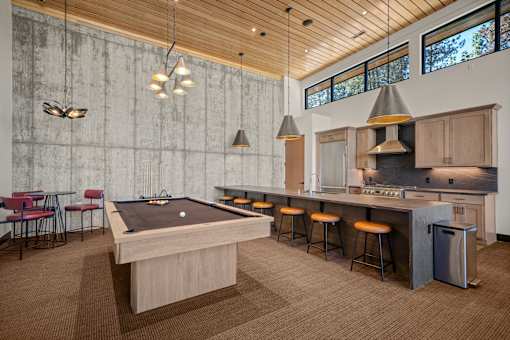 A pool table is in the middle of a room with a bar and stools.