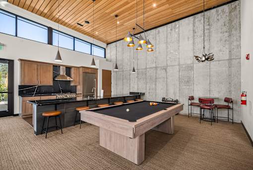 A billiards table is in the middle of a room with a bar and a kitchen.