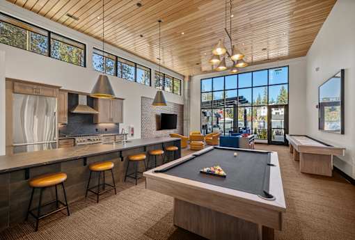 A billiard table is in the middle of a room with a kitchen area and a balcony.